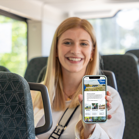 A smiling woman standing in public transport and holding a smartphone with an open mobile website. The text on the white overlay reads: 'Newsletter sign-up'