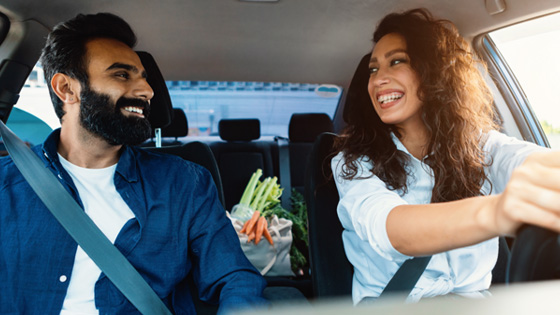 Ein lächelndes Paar im Auto mit Lebensmitteln auf dem Rücksitz 