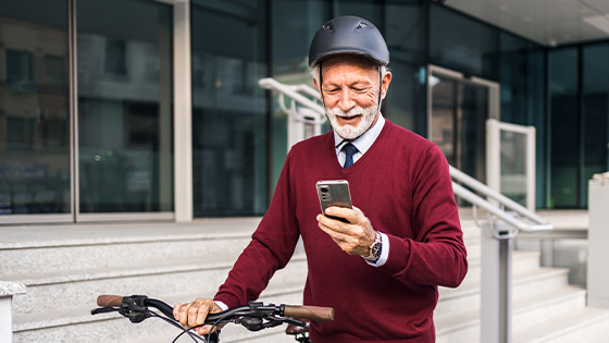 Ein alter Mann lächelt, während er mit seinem Fahrrad die Straße entlangfährt und auf sein Handy schaut
