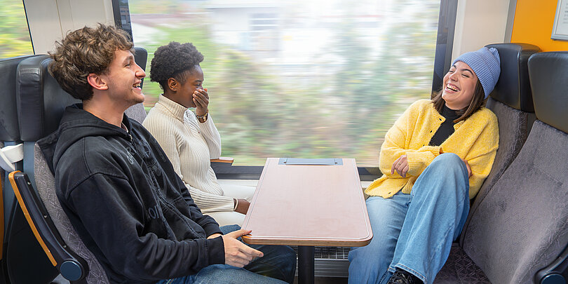 Eine Gruppe junger Menschen sitzt in einer Bahn an Tisch gegenüber.