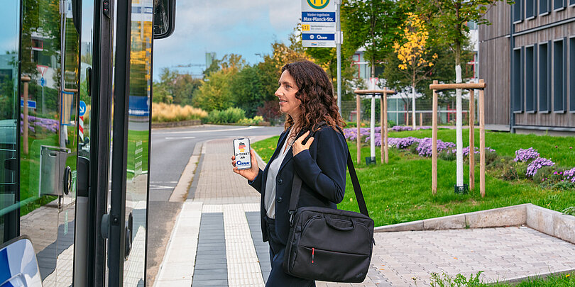 Geschäftsfrau checkt mit dem Deutschland Ticket auf dem Smartphone in den Bus ein