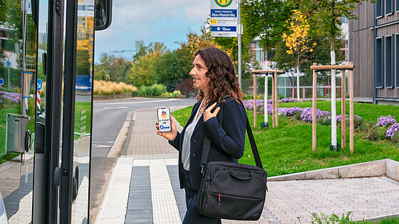 Geschäftsfrau checkt mit dem Deutschland Ticket auf dem Smartphone in den Bus ein