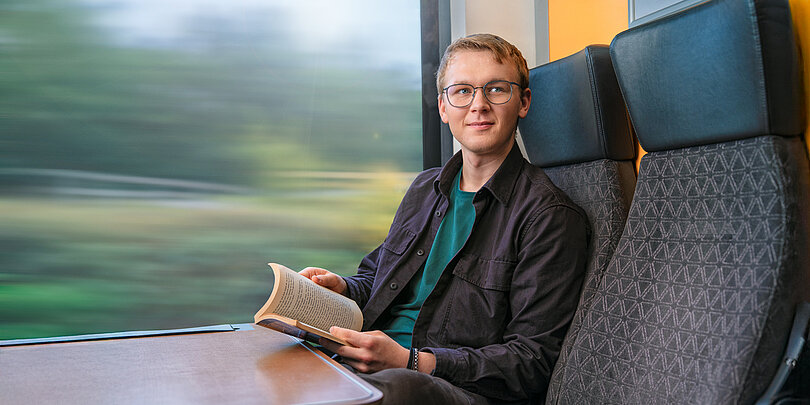 Junger Mann mit Buch im Zug