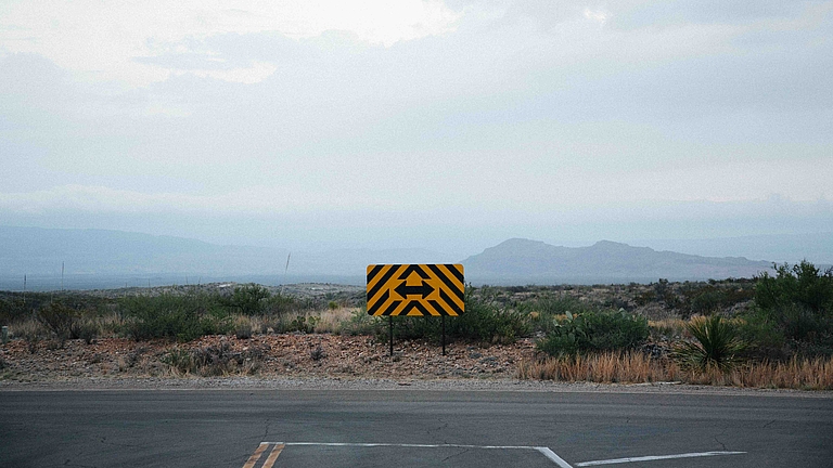 Gelbes Warnschild mit schwarzen Pfeilen auf ländlicher Straße