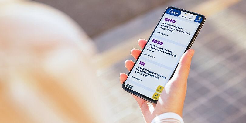 Eine Hand hält ein Mobiltelefon mit der RNN Website darauf.