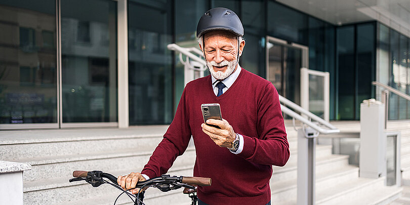 Ein alter Mann lächelt, während er mit seinem Fahrrad die Straße entlangfährt und auf sein Handy schaut