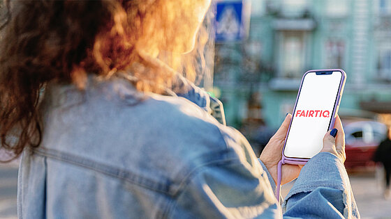 Eine Person hält ein Smartphone mit der "FAIRTIQ"-App