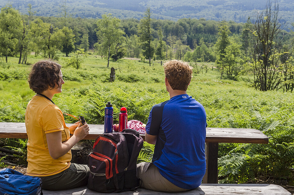 Eine Frau und ein Mann sitzen mit Rucksäcken auf einem Aussichtspunkt mit Blick über die Stadt