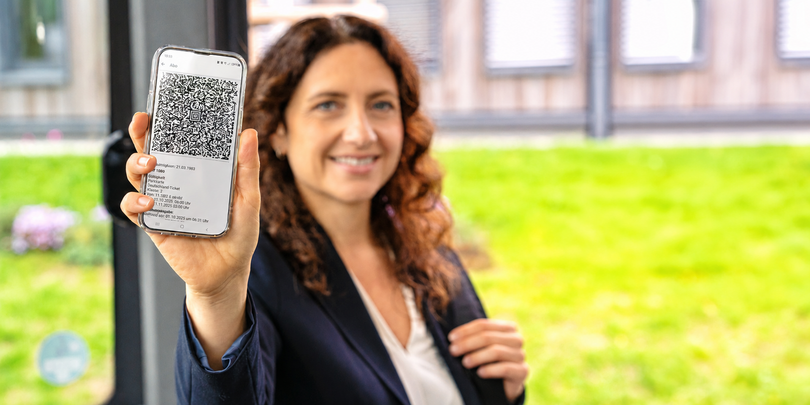 Eine Frau hält ihr Smartphone mit einem Fahrschein in die Kamera