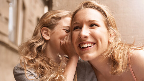 Ein Kind flüstert jemandem etwas ins Ohr.