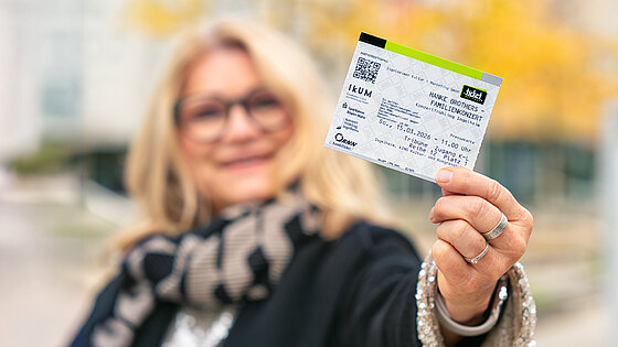 Lachende Frau hält eine Fahrkarte und das RNN-Logo in die Kamera