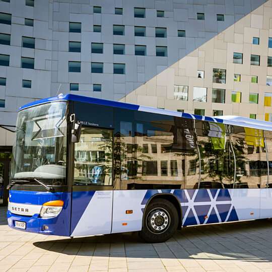 A modern, white and blue coach is parked in front of a modern office building with many windows.