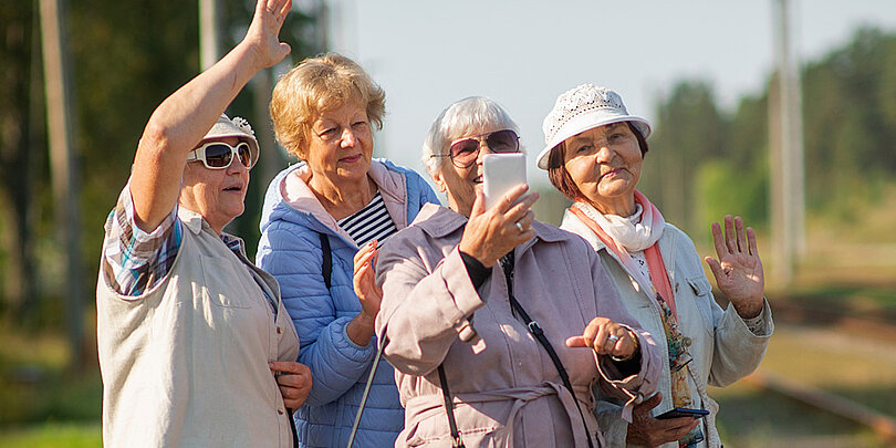 Ältere Frauen stehen im Freien und schauen lächelnd auf ein Smartphone
