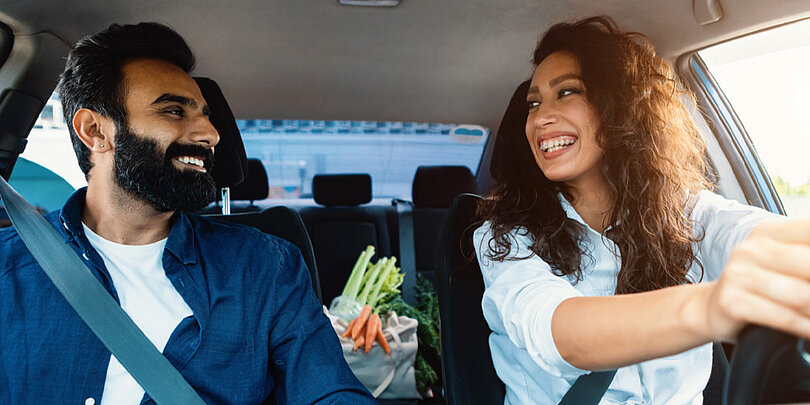 Ein lächelndes Paar im Auto mit Lebensmitteln auf dem Rücksitz 