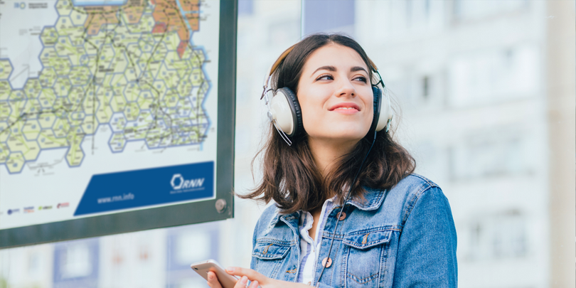 Frau steht mit Handy in der Hand vor Fahrplan