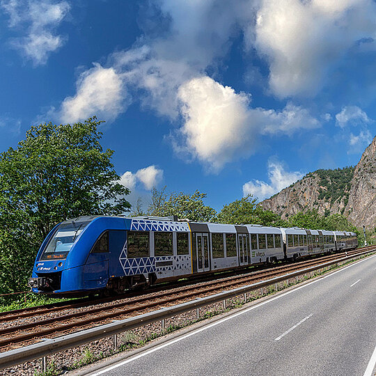 Blue regional train on tracks in a green landscape under a light blue sky with white clouds