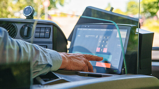 Nahaufnahme: Hand eines Busfahrers bedient den Touchscreen des Fahrkarten- und Bordrechners