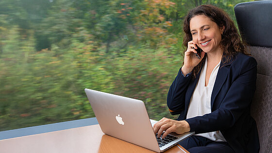 Frau im Zug telefoniert und hat einen Laptop vor sich.